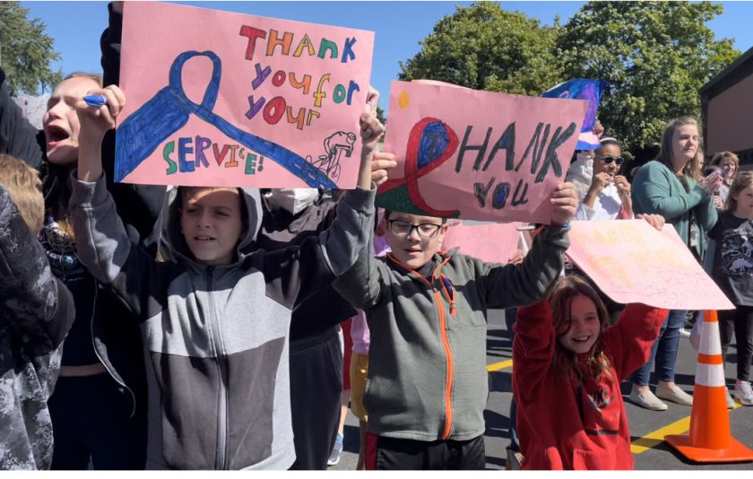 students standing outside holding a signs and cheering