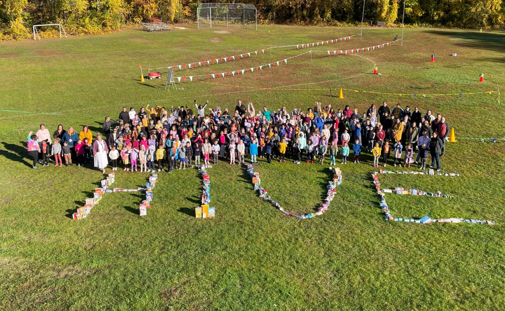 students gathered out on the field with the word HIVE spelled out on the ground with food collected