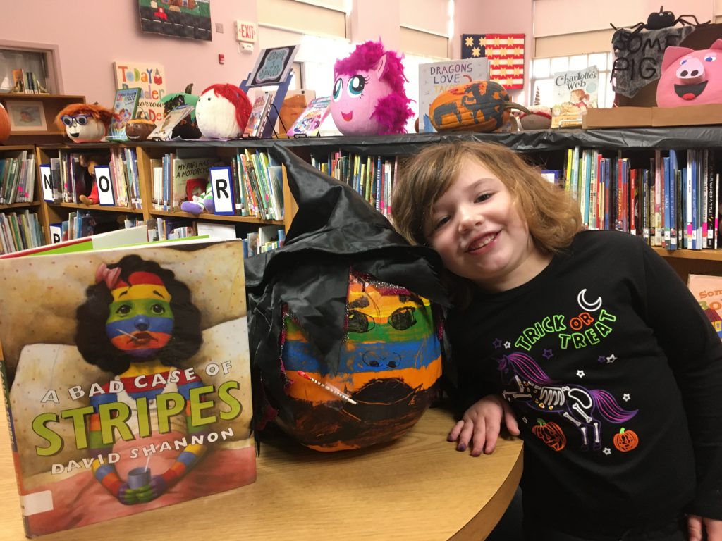 student pops head in close to her decorated pumpkin