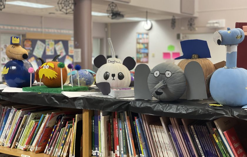 pumpkins decorated like pandas and elephants and other book characters displayed on library bookshelf
