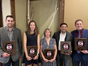 five people standing in a line and each are holding a plaque