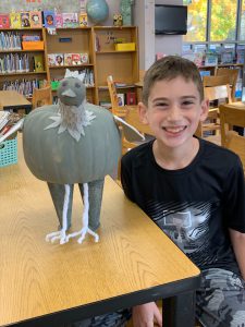 students smiling next to a bird creation he made out of a pumpkin