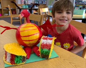 student sits proudl next to red dragon he made out of a pumpkin surrounded by two tacos