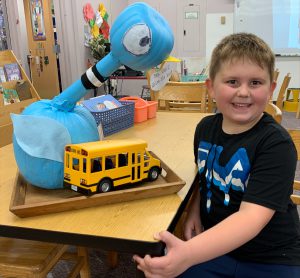 student sitting next to a creation he made out of pumpkins - a pigeon and he put a school bus next to it