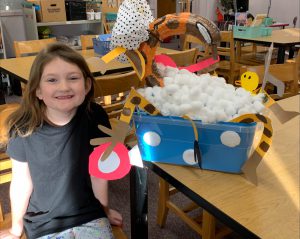 student next to her art for giraffe in a bath made out of pumpkins and cotton balls and construction paper and more