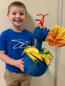 student holding dragon he made out of a pumpkin he painted blue with paper tacos and fire breathing tissue paper