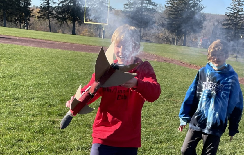 student holds rocket with smoke coming out of the bottom of it