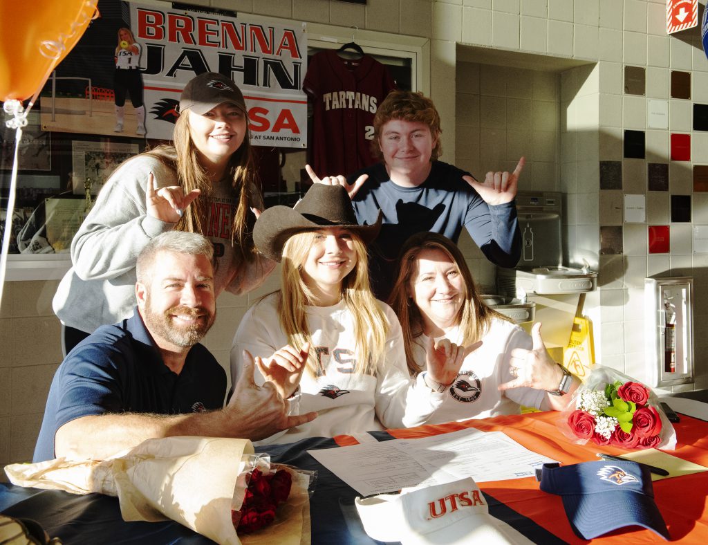 student sits with her parents and family at a table with their pinkies and thumbs up