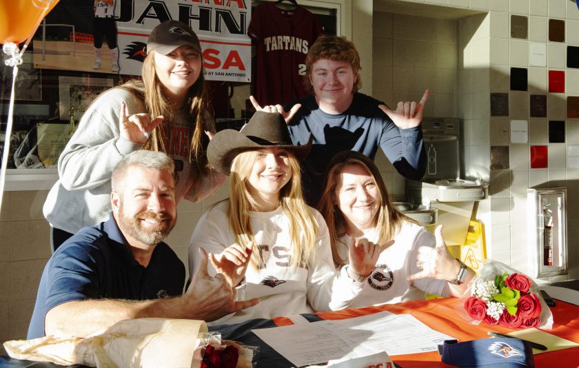 student sits with her parents and family at a table with their pinkies and thumbs up
