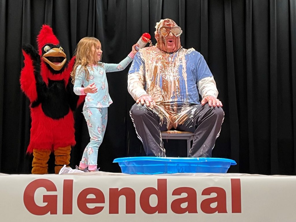 cardinal mascot, student dumping sprinkles on her principal sitting on stage