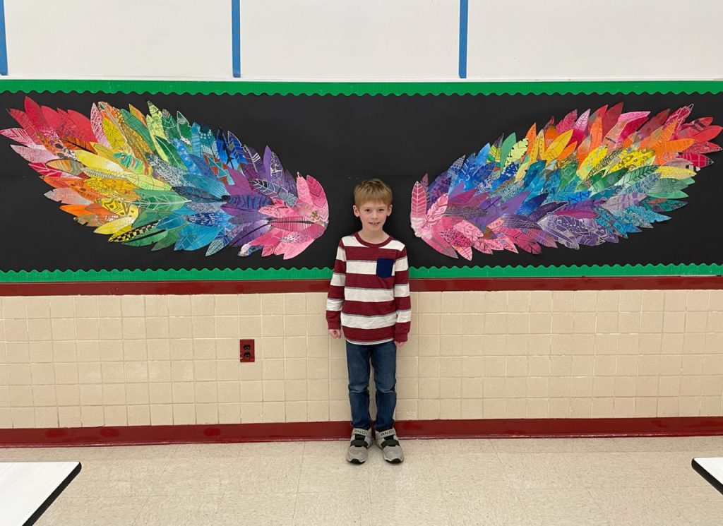 student standing in front of wings made from colorful feathers