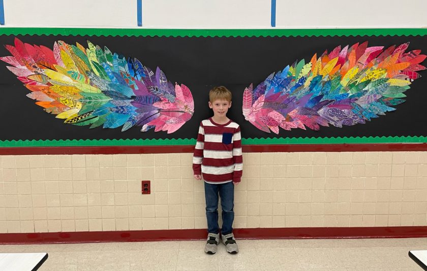 student standing in front of wings made from colorful feathers