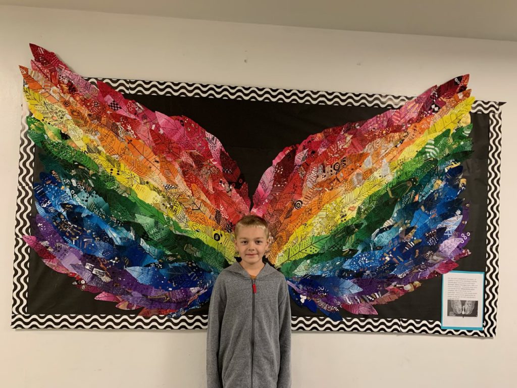 student standing in front of wings made out of colorful feathers