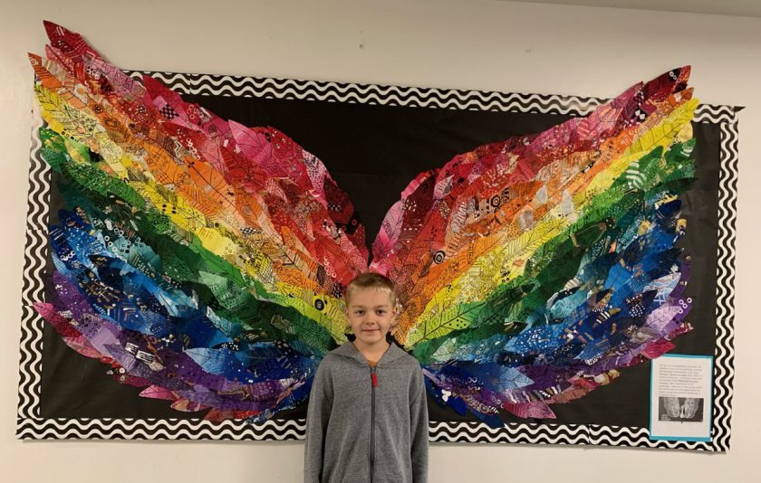 student standing in front of wings made out of colorful feathers