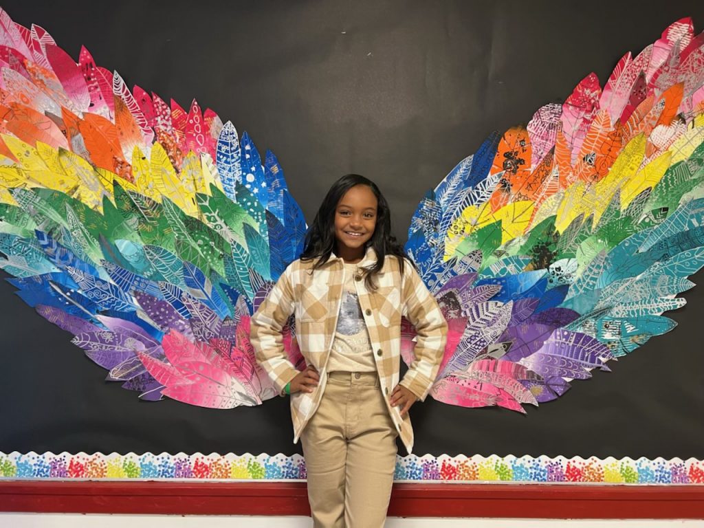 student standing in front of butterfly wings made of unique feathers