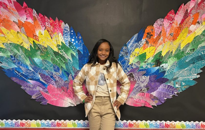 student standing in front of butterfly wings made of unique feathers