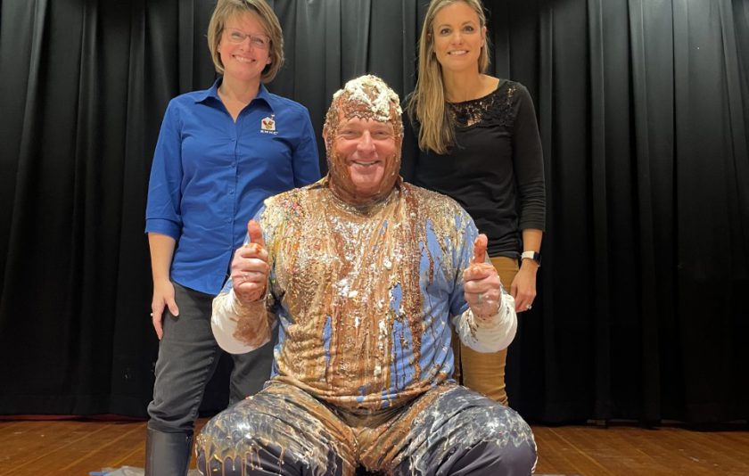 two women standing behind principal with sauces dumped all over him