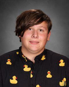 student with brown hair swooped to side wearing a dark shirt with yellow ducks