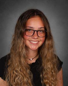 student with long brown hair and black framed glasses