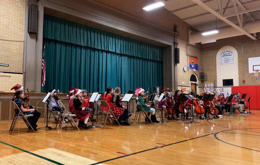 students sitting in fold out chairs on gym floor holding instruments