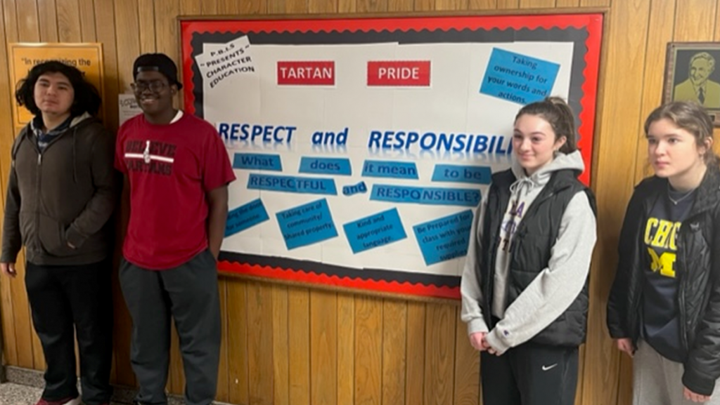 four students standing near a respect and responsibility banner