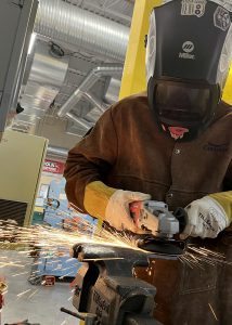 student wearing protective gear has both hands up welding metal