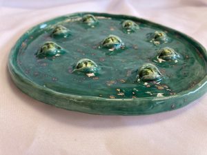 a green circular ceramic with bubbles that look like eyeballs on the top