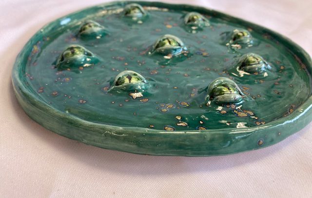 a green circular ceramic with bubbles that look like eyeballs on the top