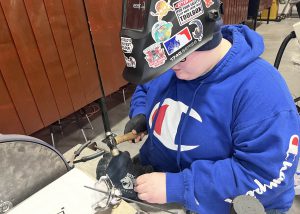student wearing a protective helmet using a hammer to make a metal rose