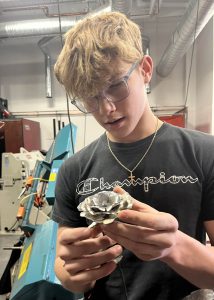 student wearing goggles holds a silver colored rose made out of metal