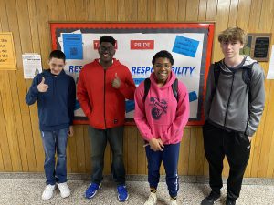 four students standing together and the first two are giving a thumbs up pose