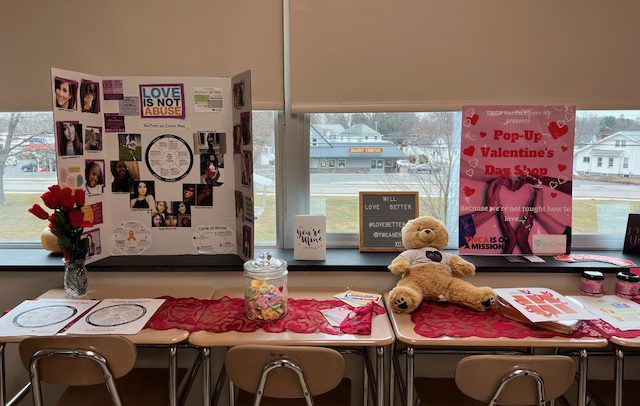candy and a teddy bear on the table and posters behind that stating that love is not abuse