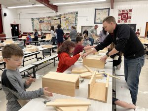 students wearing goggles sitting at tables putting together toolboxes made out of wood