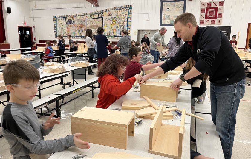 students wearing goggles sitting at tables putting together toolboxes made out of wood