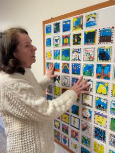 woman touches tiles of artwork hung on the wall