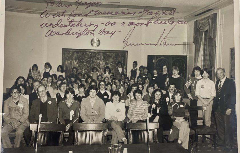 an old photo from 1979, where students and adults are sitting together in chairs and some are standing looking forward at the camera