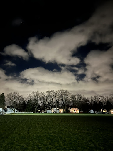 A night sky with clouds and a lit up small town neighborhood below