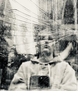 a person looking at their reflection in a window with broken glass