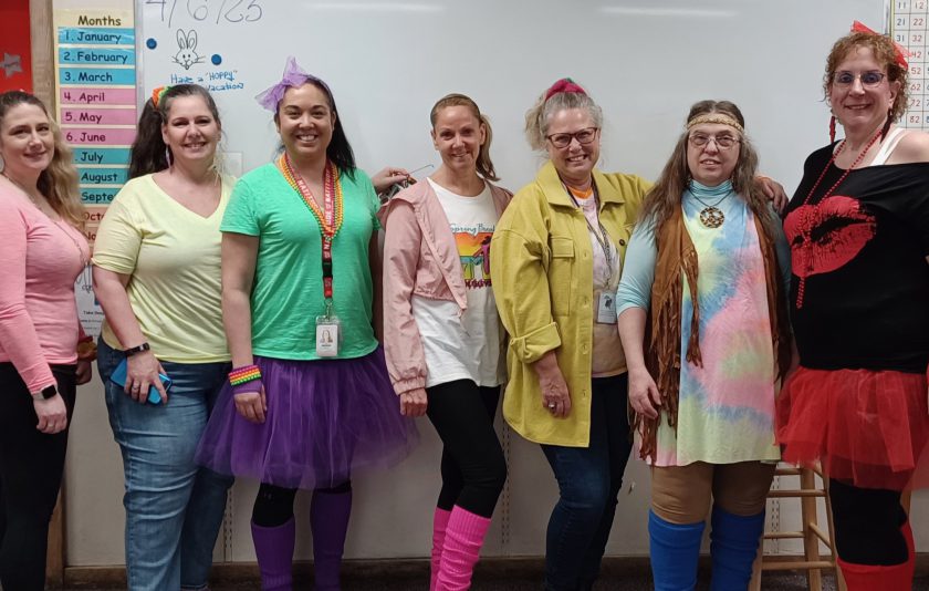 seven women standing in a line wearing decade look costumes