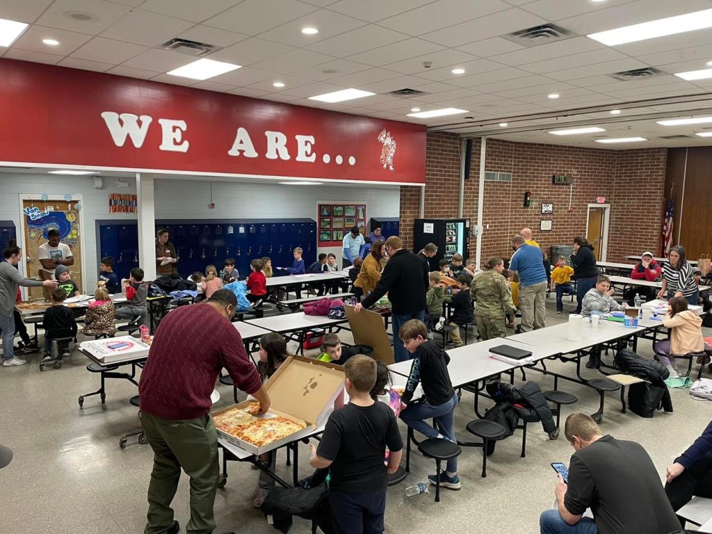 students and adults in a school cafeteria having a pizza party