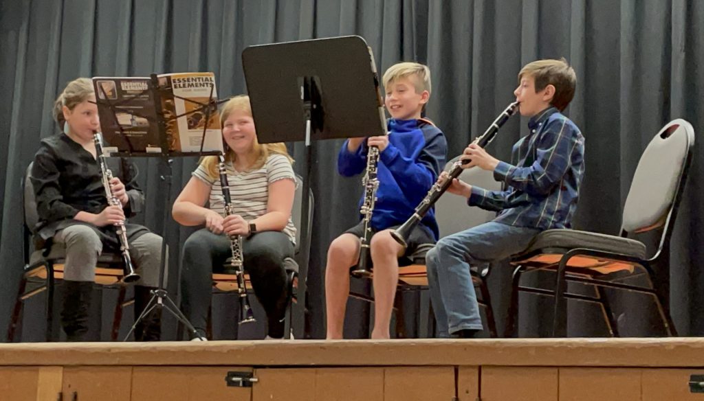 four students on stage sitting down with their instruments