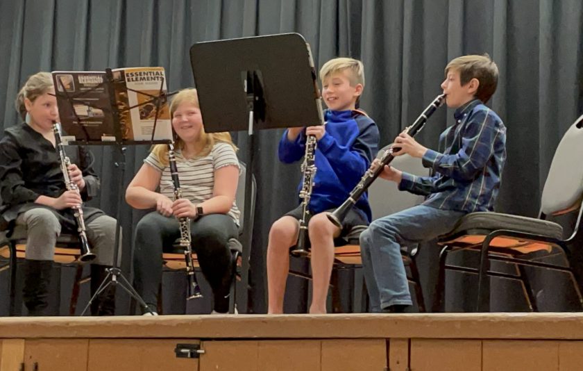 four students on stage sitting down with their instruments