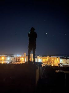 shadow of person standing on top of building with lights from big buildings down below.