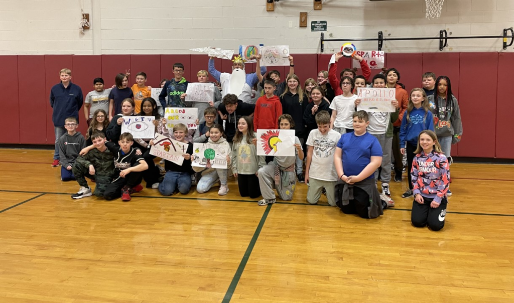 students piled up in a gymnasium holding handmade flags