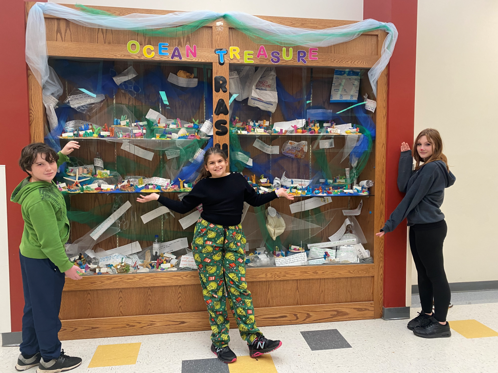 three students standing by a large case with colorful art pieces behind the glass