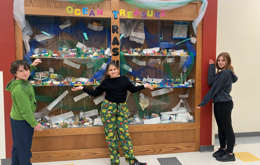 three students standing by a large case with colorful art pieces behind the glass