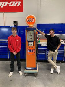 two students stand next to newly restored orange gas pump