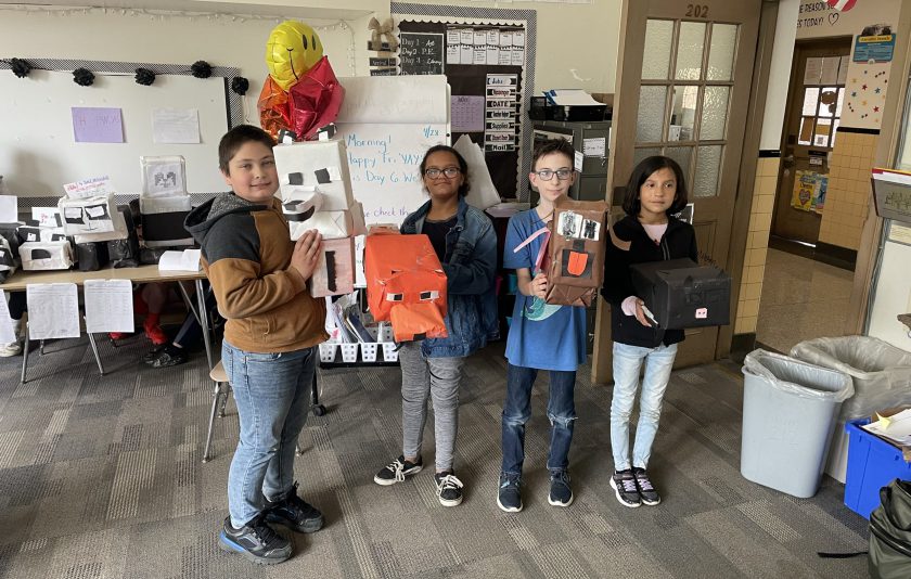 four students standing with boxes they made into animals