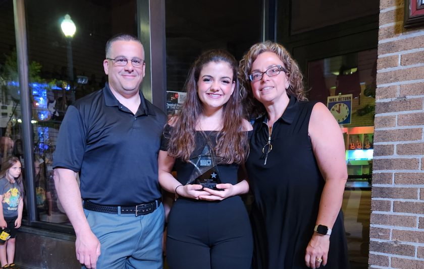 student holding a glass star for Best Actress award is standing between her parents