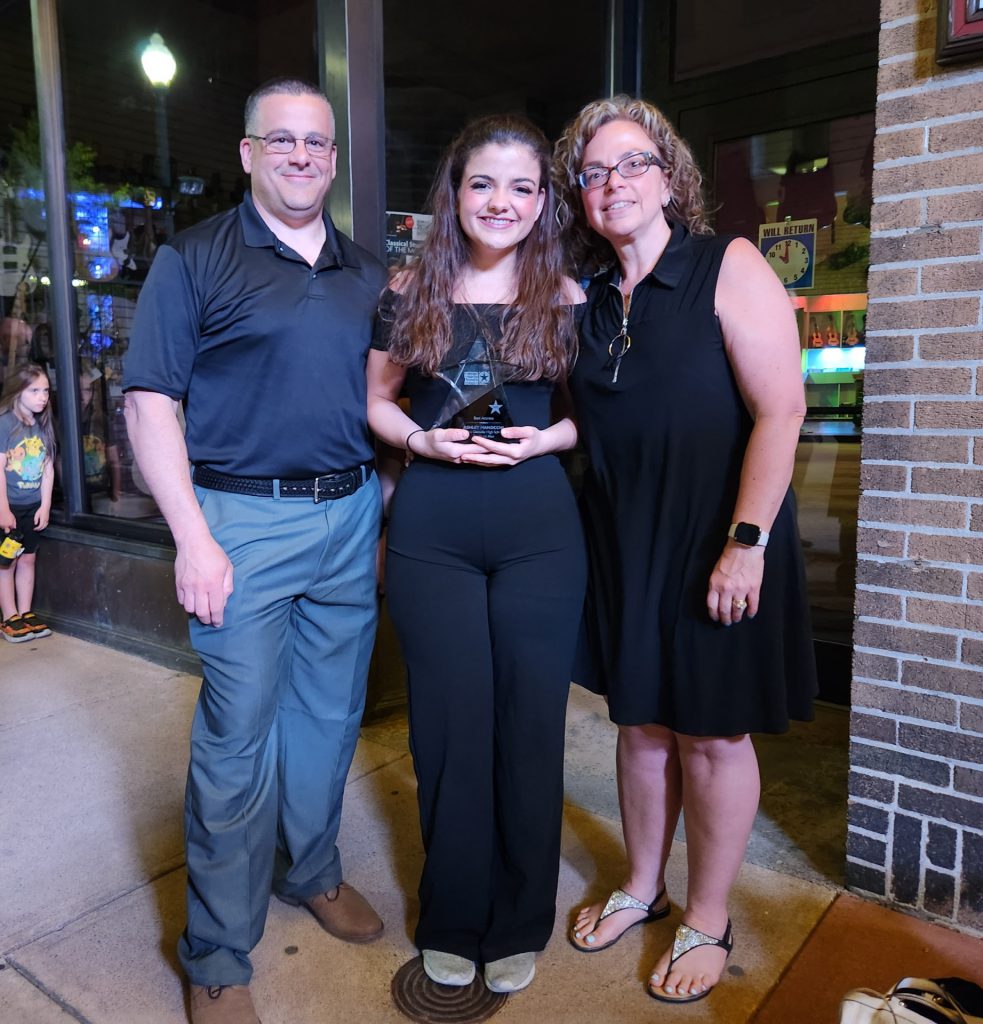 student holding a glass star for Best Actress award is standing between her parents